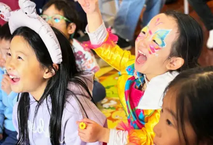Joyful children at a party with colorful face paint, cheering and smiling.